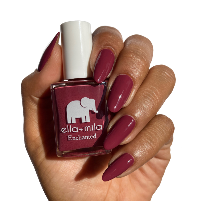 Rise of Petals berry burgundy nail polish on a deep skin tone, holding the bottle